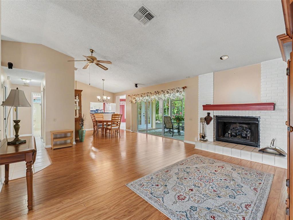 A spacious living room with wood flooring, a white brick fireplace, and a dining area — 3341 PLAYER DRIVE, NEW PORT RICHEY, FL