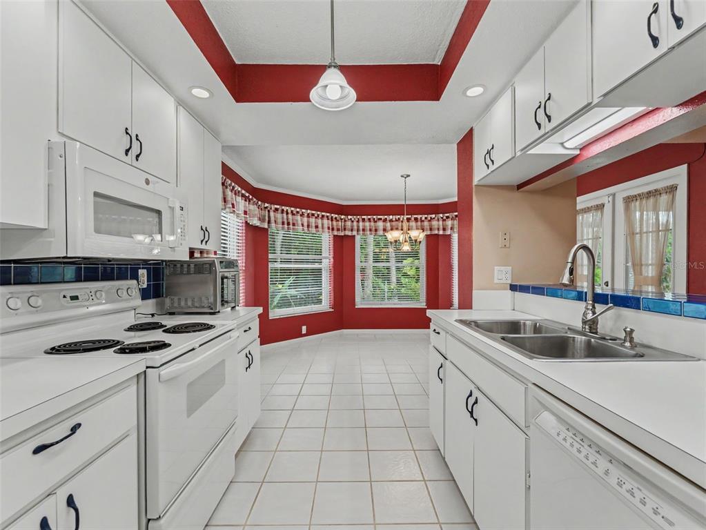 A kitchen with white cabinets, white appliances, red walls, and a tiled floor — 3341 PLAYER DRIVE, NEW PORT RICHEY, FL