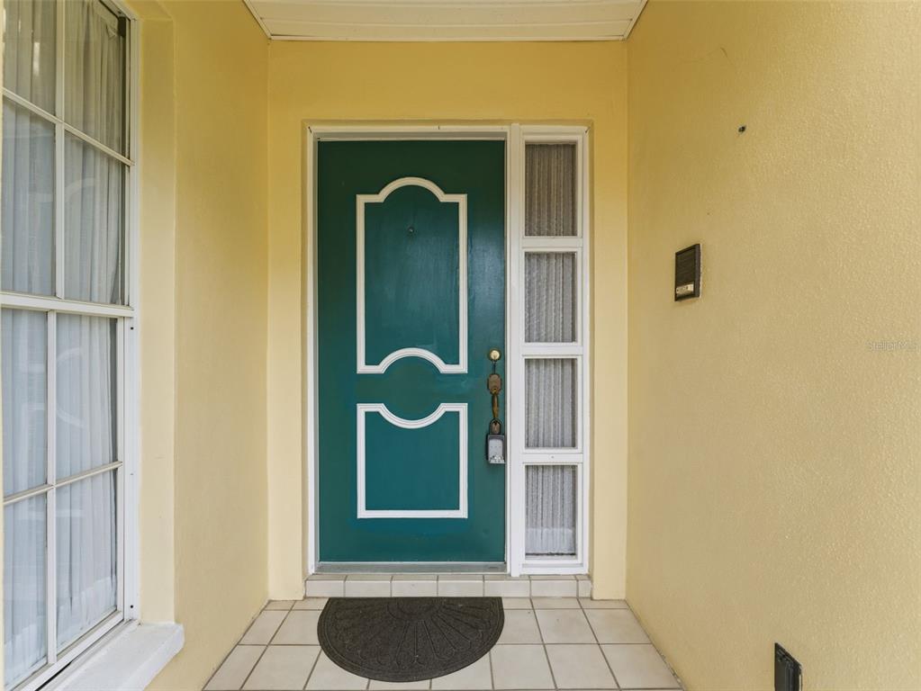 A green front door with white trim sits under a covered entryway with tiled flooring — 3341 PLAYER DRIVE, NEW PORT RICHEY, FL