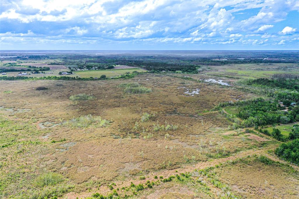 An aerial view shows a vast, flat landscape of marshland, scattered trees, and distant rural buildings — 3386 MAPLE LANE, HAINES CITY, FL