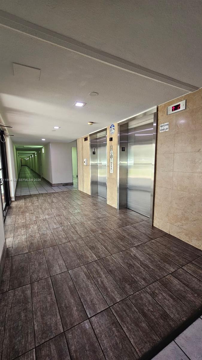 A hallway with wood-look tile flooring leads to two stainless steel elevator doors — 8075 NW 7th St # 401, Miami FL 33126, MIAMI, FL