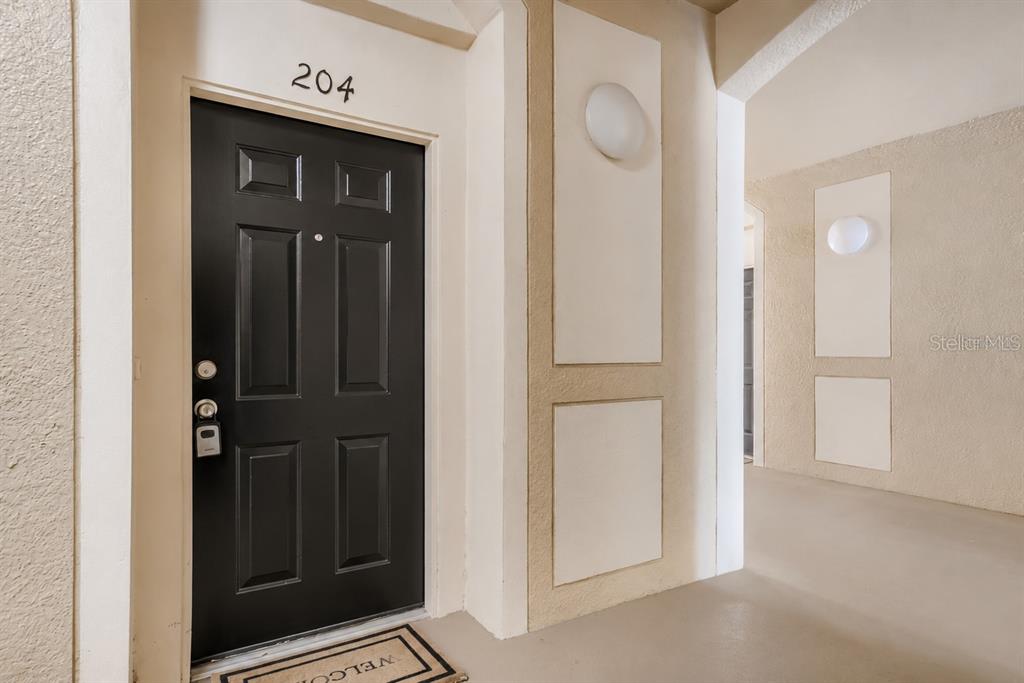 A black front door labeled 204 is set in a beige stucco hallway — 2484 SAN TECLA STREET UNIT 204, ORLANDO, FL