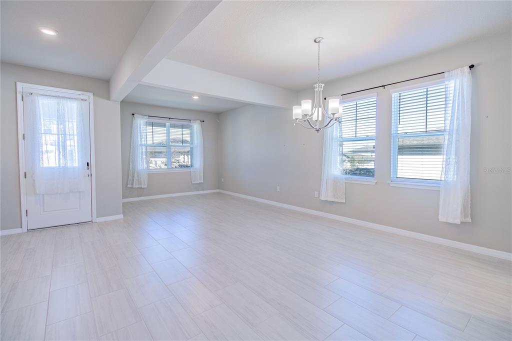 An empty room with light-colored tile flooring, a chandelier, and several windows with curtains — 2290 RAVEN RIDGE ROAD, CLERMONT, FL