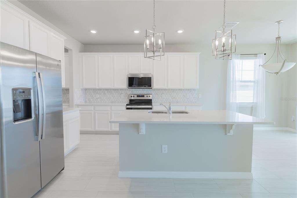 A modern kitchen features white cabinetry, stainless steel appliances, and a large central island — 2290 RAVEN RIDGE ROAD, CLERMONT, FL