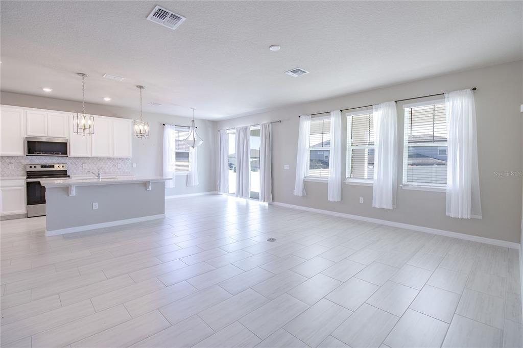 A bright, open-concept kitchen and living area features white cabinetry, tile flooring, and large windows — 2290 RAVEN RIDGE ROAD, CLERMONT, FL