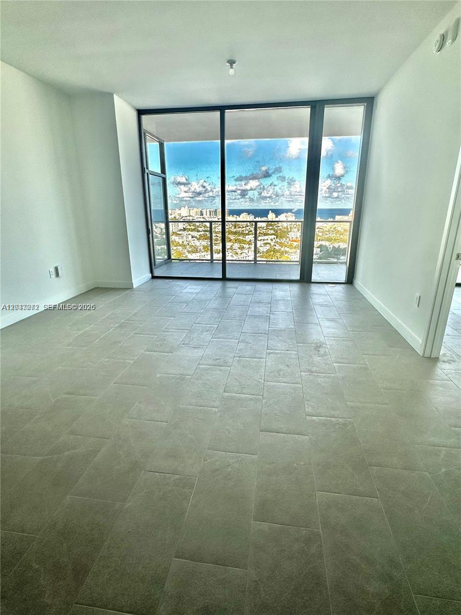 An empty room with gray tile flooring features floor-to-ceiling windows overlooking the ocean — 500 Alton Rd # 2108, Miami Beach FL 33139, MIAMI BEACH, FL