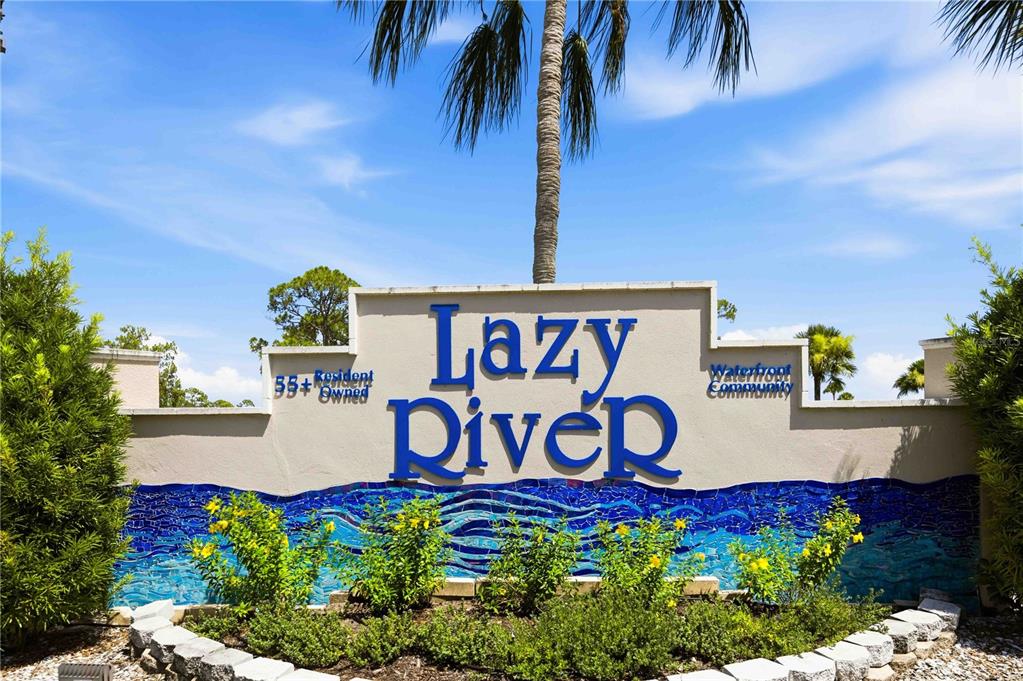 A sign for Lazy River, a 55+ resident-owned waterfront community, stands outdoors under a palm tree — 206 TORTOLA WAY, NORTH PORT, FL
