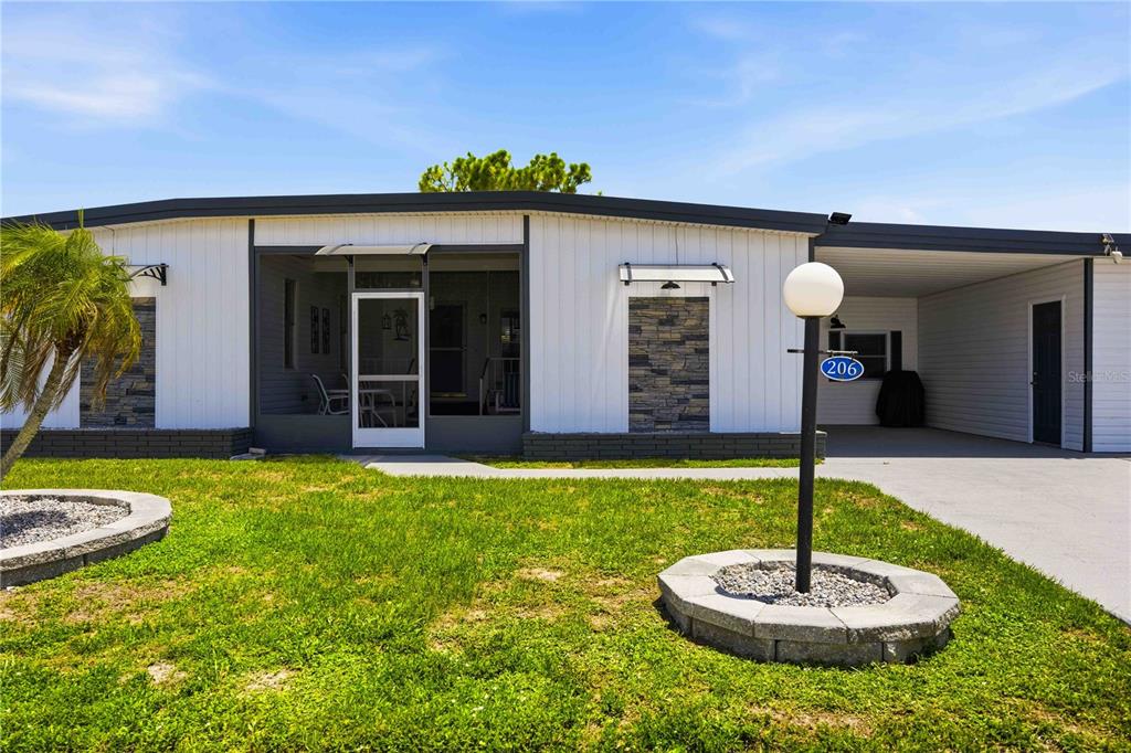 A single-story manufactured home with a screened front porch, carport, and stone-accented exterior walls — 206 TORTOLA WAY, NORTH PORT, FL