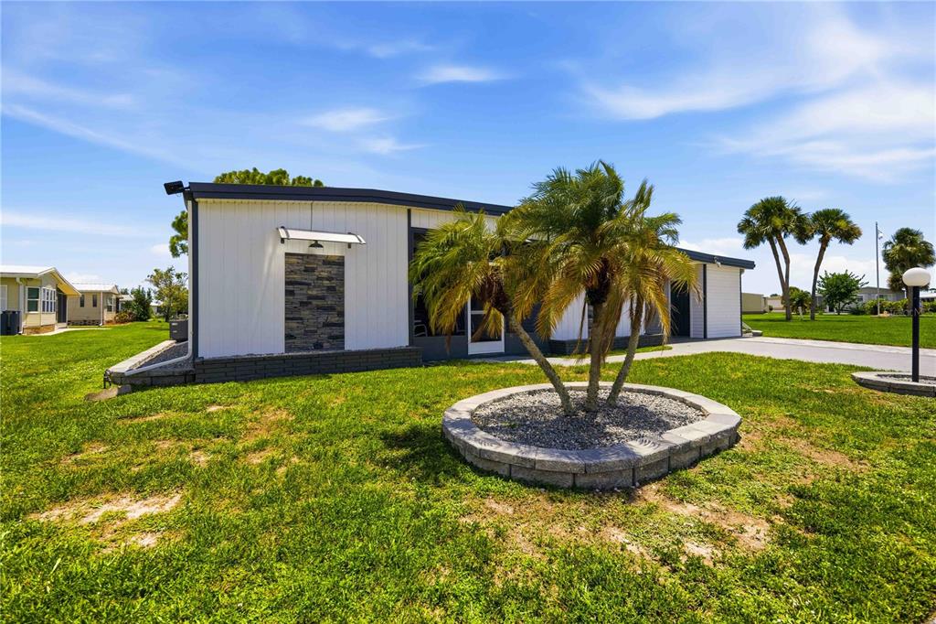 A single-story manufactured home with a stone accent wall and a palm tree in front — 206 TORTOLA WAY, NORTH PORT, FL