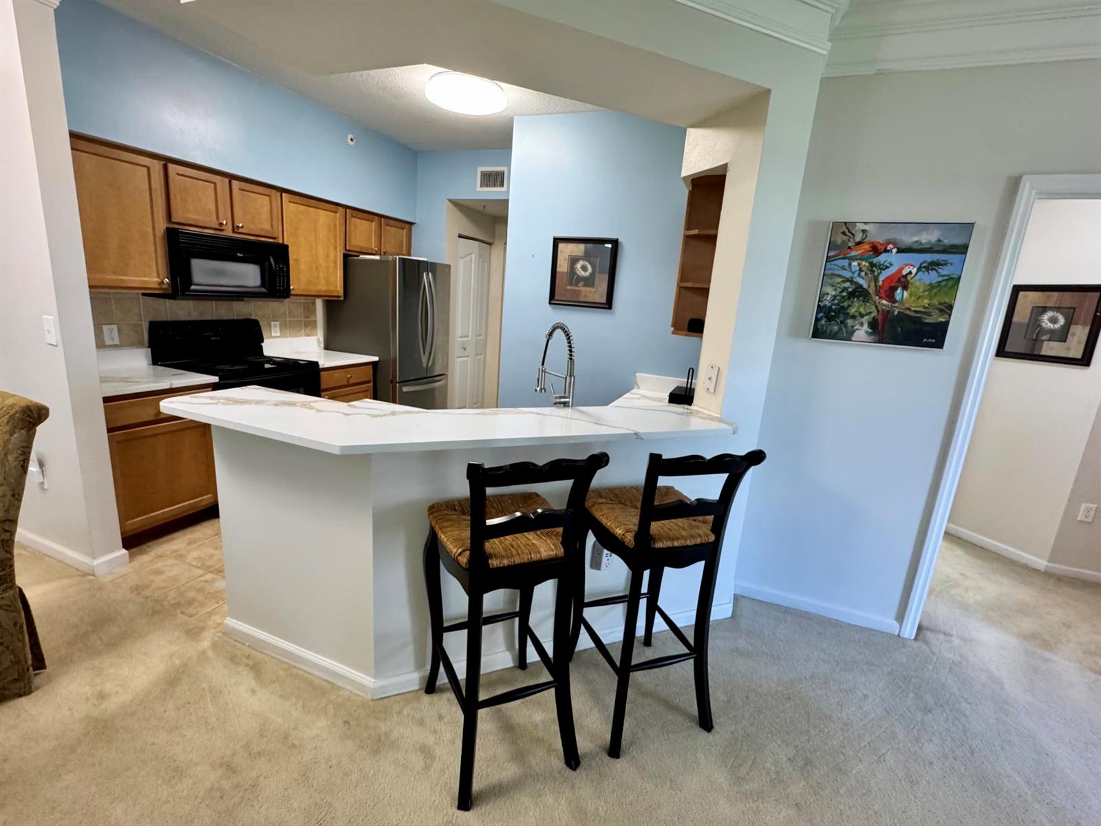A kitchen features light blue walls, wooden cabinets, stainless steel appliances, and a white countertop — 9857 Baywinds # 9210, West Palm Beach FL 33411, WEST PALM BEACH, FL