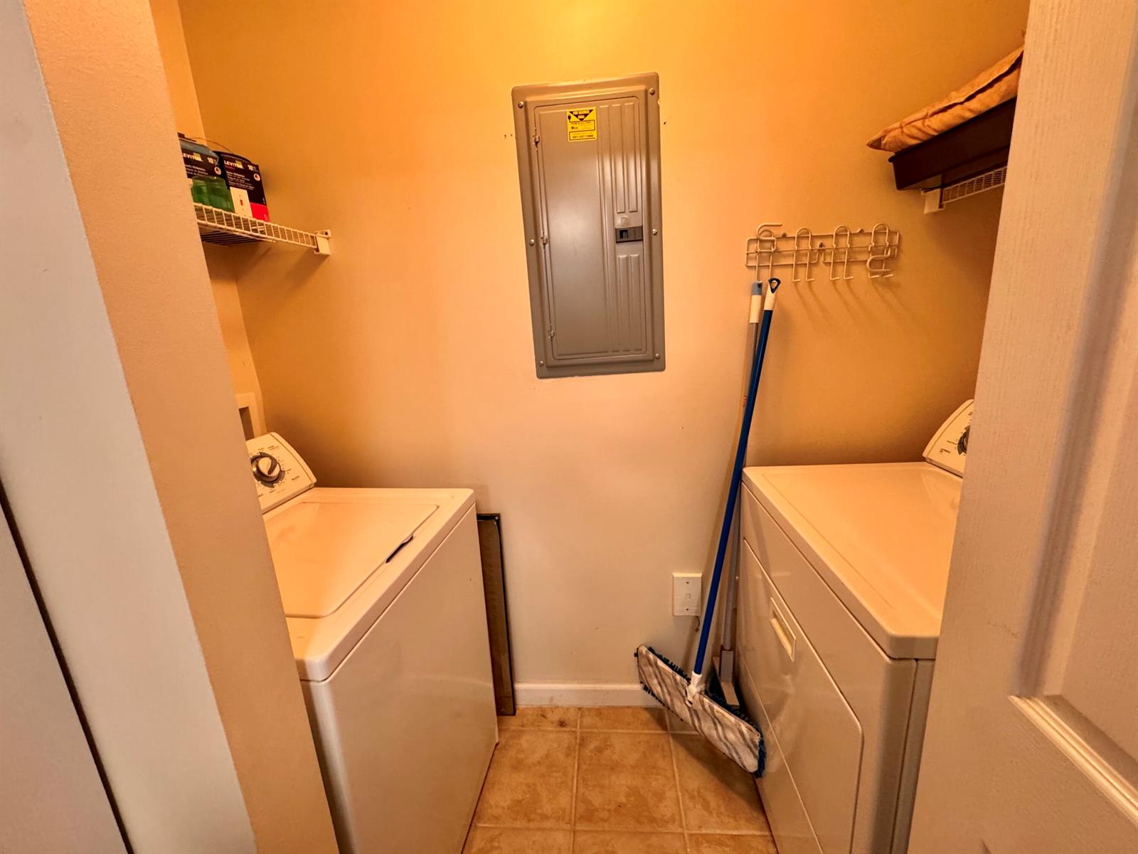 A laundry closet contains a washer, dryer, electrical panel, and wall-mounted storage shelving — 9857 Baywinds # 9210, West Palm Beach FL 33411, WEST PALM BEACH, FL