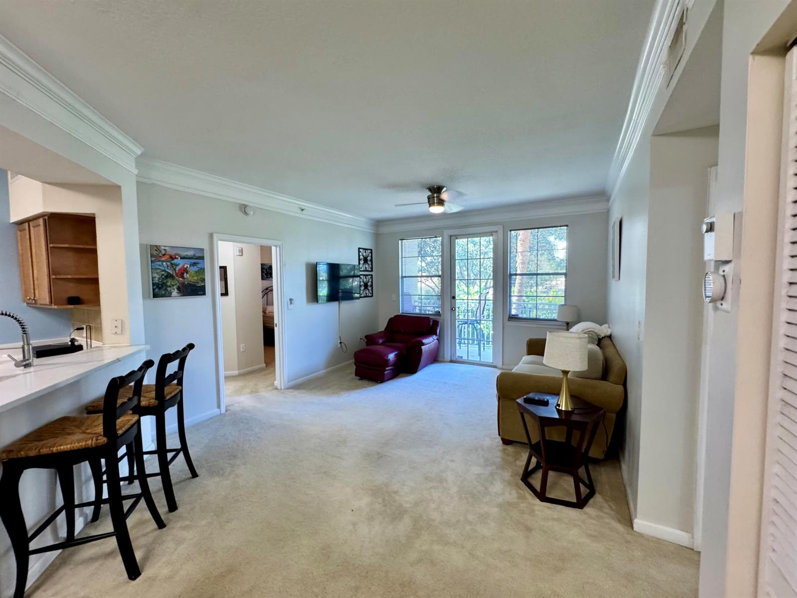 A living room features beige carpeting, a tan sofa, a red recliner, and a breakfast bar — 9857 Baywinds # 9210, West Palm Beach FL 33411, WEST PALM BEACH, FL