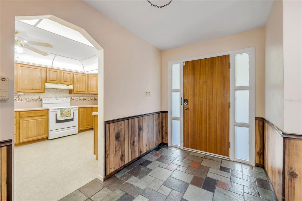 An entryway with wood paneling and slate tile flooring leads into a kitchen with oak cabinets — 1428 MARDRAKE ROAD, DAYTONA BEACH, FL