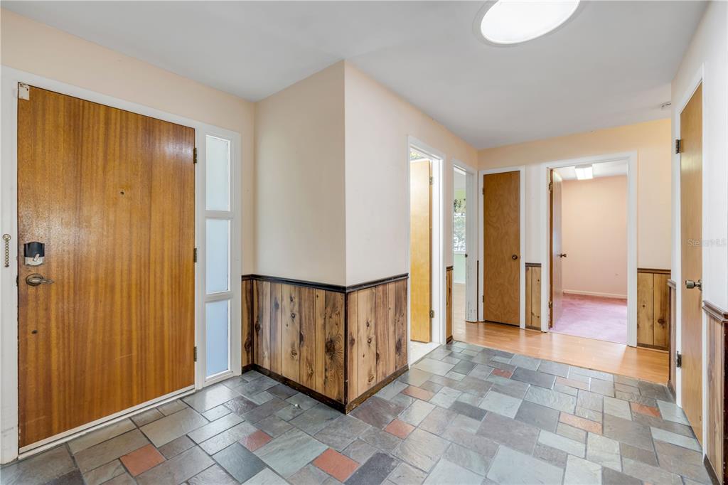 An entryway with slate tile flooring, wood paneling, and multiple interior doors — 1428 MARDRAKE ROAD, DAYTONA BEACH, FL