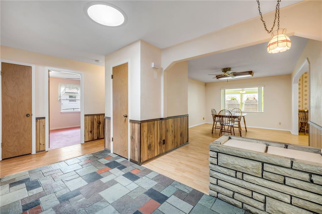A room with stone-look tile flooring, wood wainscoting, and an adjacent dining area with wood floors — 1428 MARDRAKE ROAD, DAYTONA BEACH, FL
