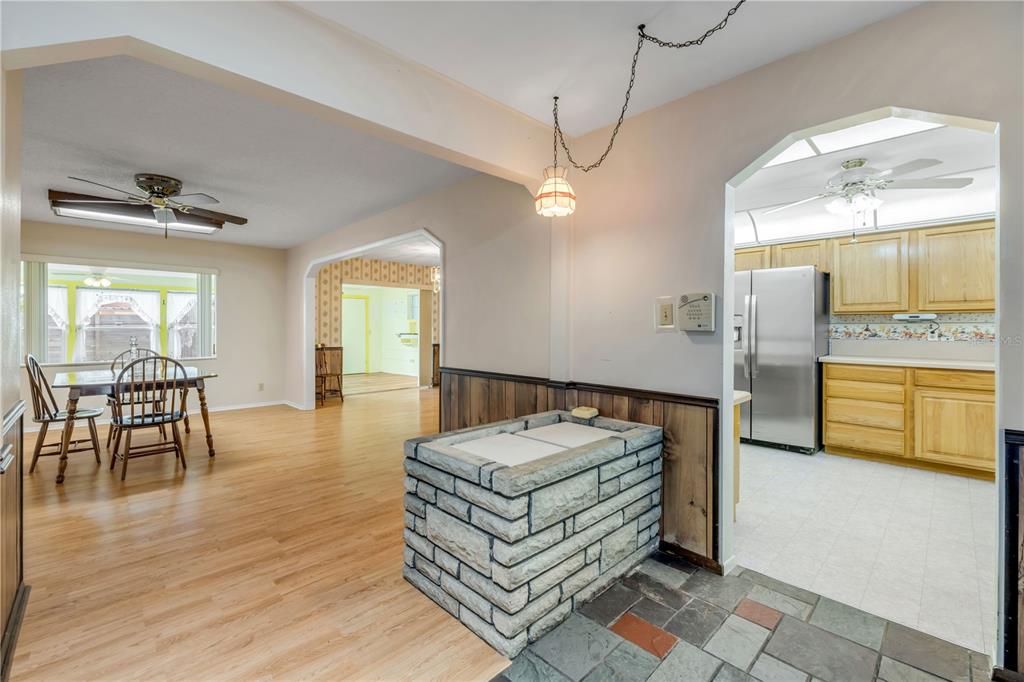 A dining area with wood flooring leads to a kitchen featuring light wood cabinets — 1428 MARDRAKE ROAD, DAYTONA BEACH, FL