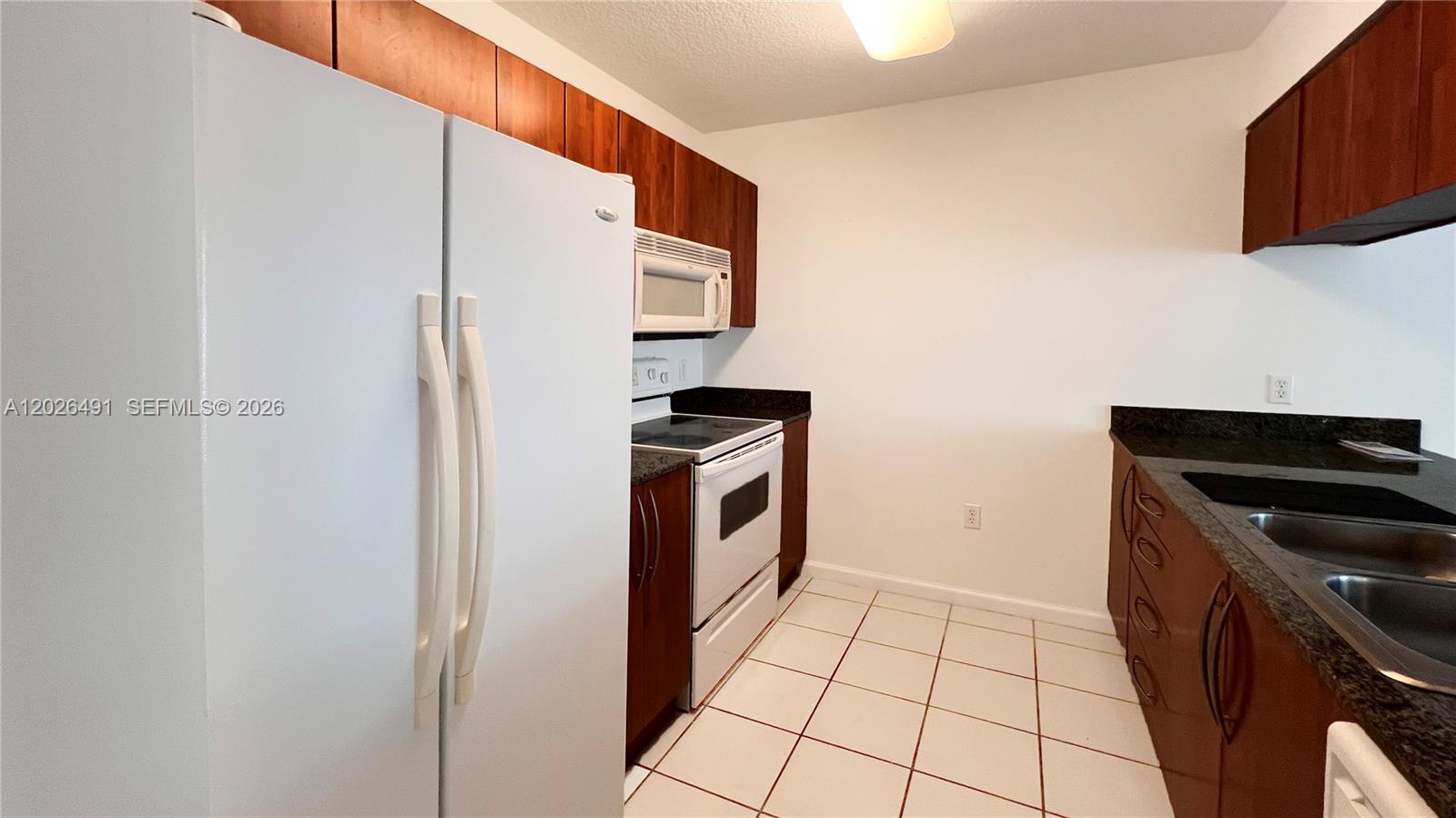 A kitchen features white appliances, dark wood cabinets, granite countertops, and white tile flooring — 1200 Brickell Bay Dr # 2814, Miami FL 33131, MIAMI, FL