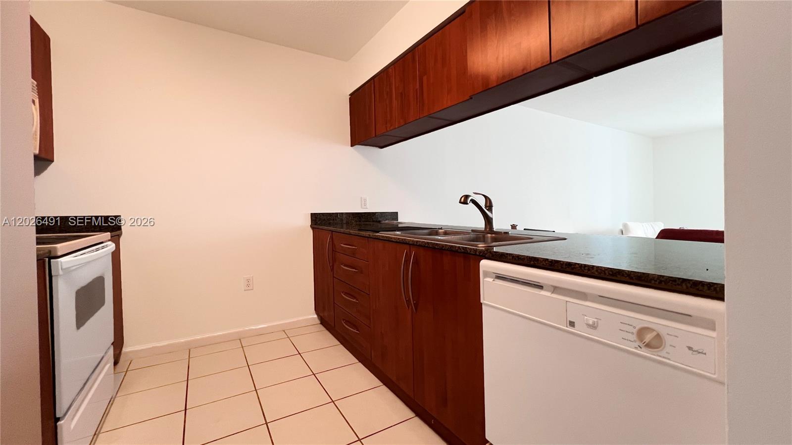 A kitchen features dark wood cabinets, a white dishwasher, a white stove, and tile flooring — 1200 Brickell Bay Dr # 2814, Miami FL 33131, MIAMI, FL