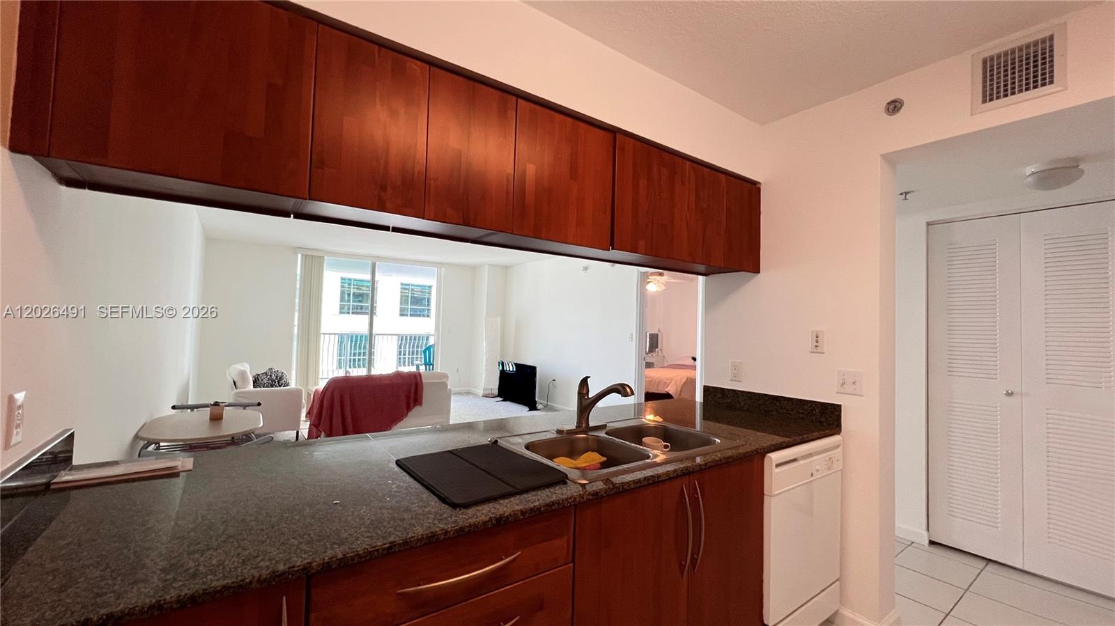 A kitchen with dark wood cabinets and granite countertops overlooks a living area — 1200 Brickell Bay Dr # 2814, Miami FL 33131, MIAMI, FL