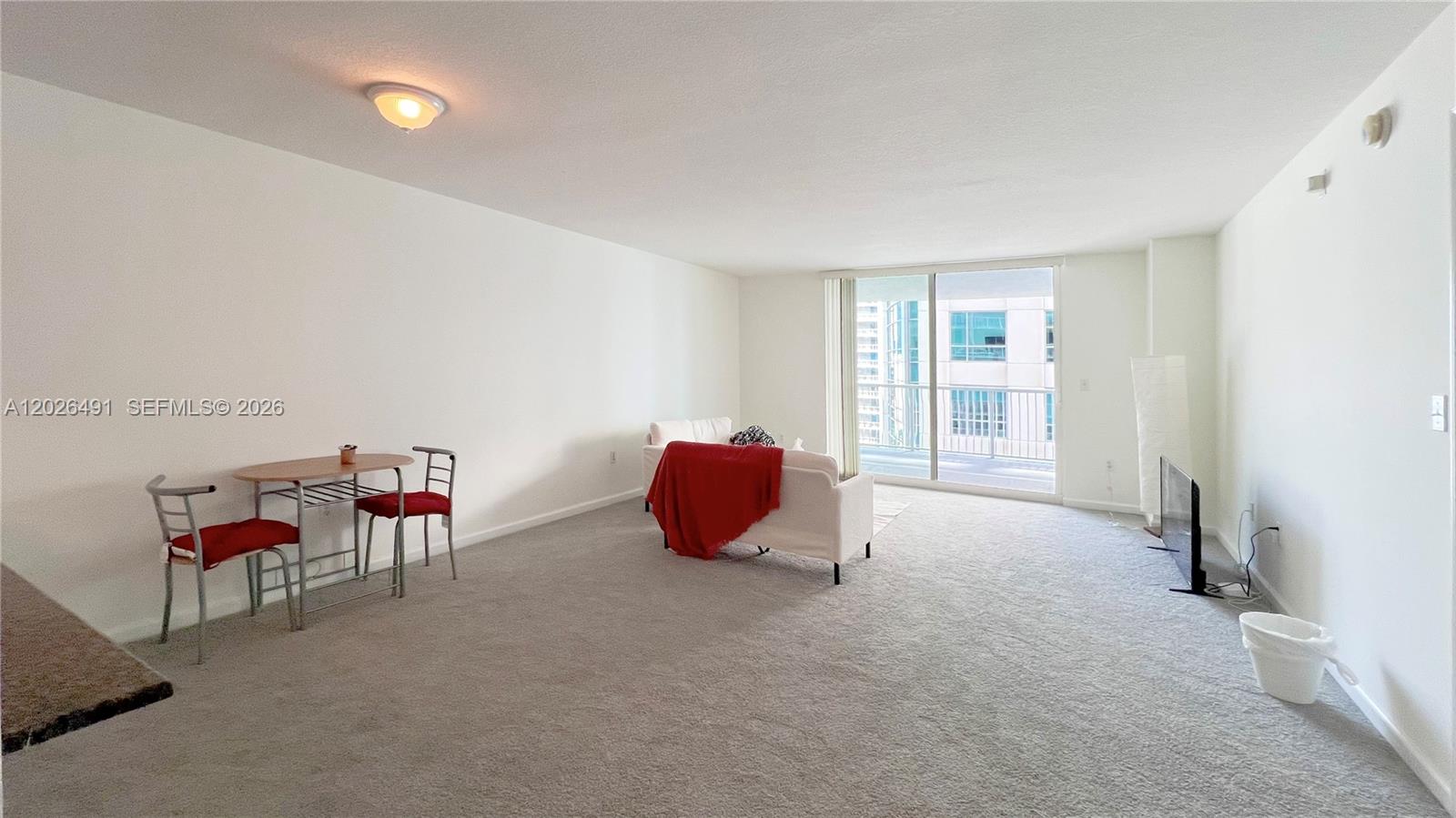 A living room features gray carpeting, white walls, a small dining set, and a balcony — 1200 Brickell Bay Dr # 2814, Miami FL 33131, MIAMI, FL