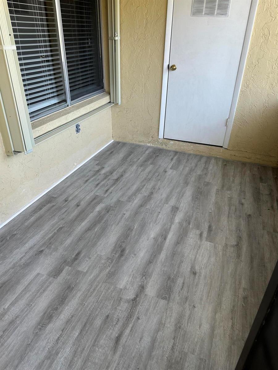 A balcony with gray wood-look flooring, a window with blinds, and a white door — 436 Pine Glen Lane # 1, FL 33463, FL