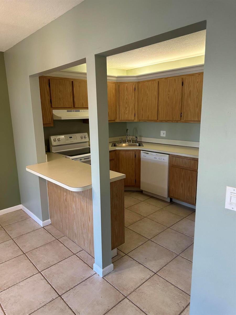 A kitchen with oak cabinets, a breakfast bar, and tile flooring viewed through a doorway — 436 Pine Glen Lane # 1, FL 33463, FL
