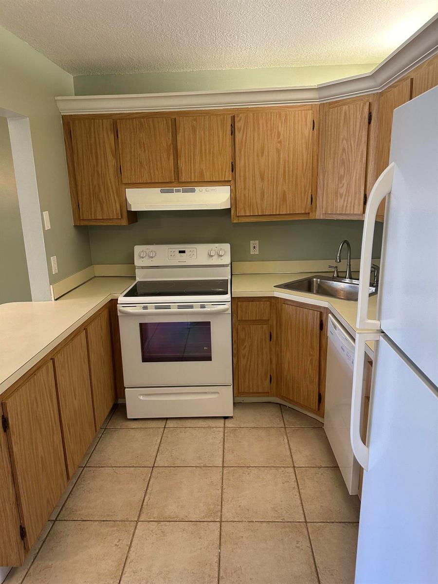 A kitchen features oak cabinets, white appliances, beige countertops, and light-colored tile flooring — 436 Pine Glen Lane # 1, FL 33463, FL