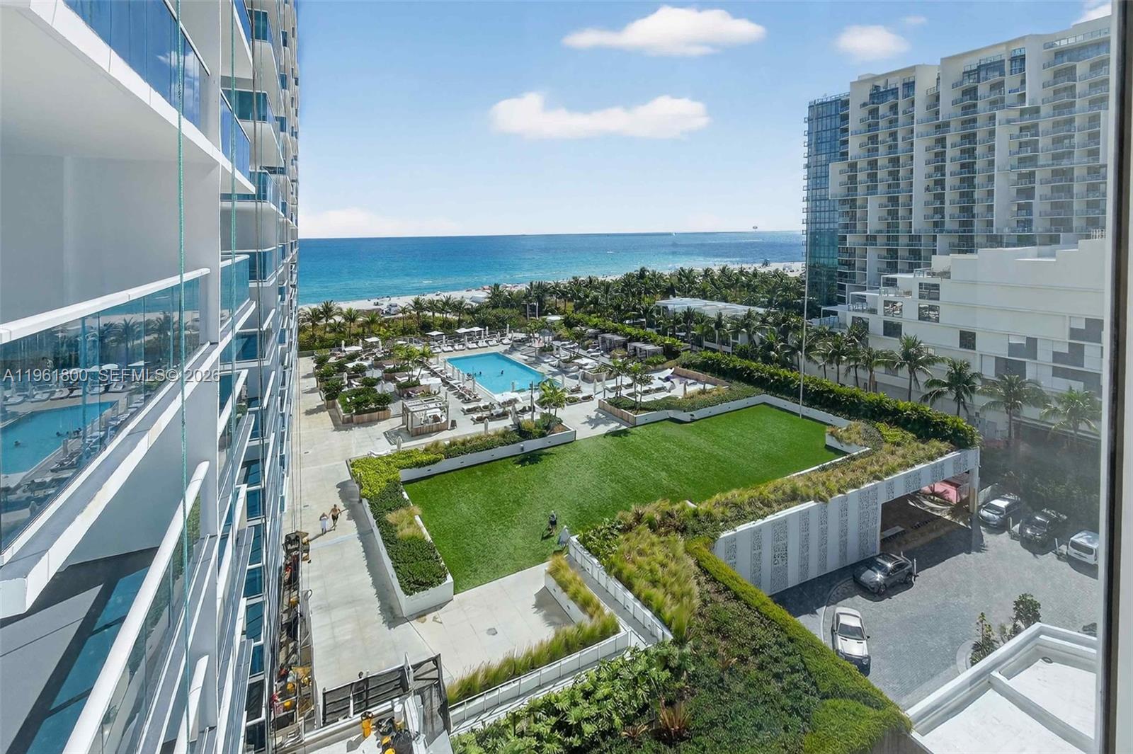 An elevated view shows a grassy courtyard, swimming pool, and beach beyond a modern building — 2301 Collins Ave # 943, Miami Beach FL 33139, MIAMI BEACH, FL