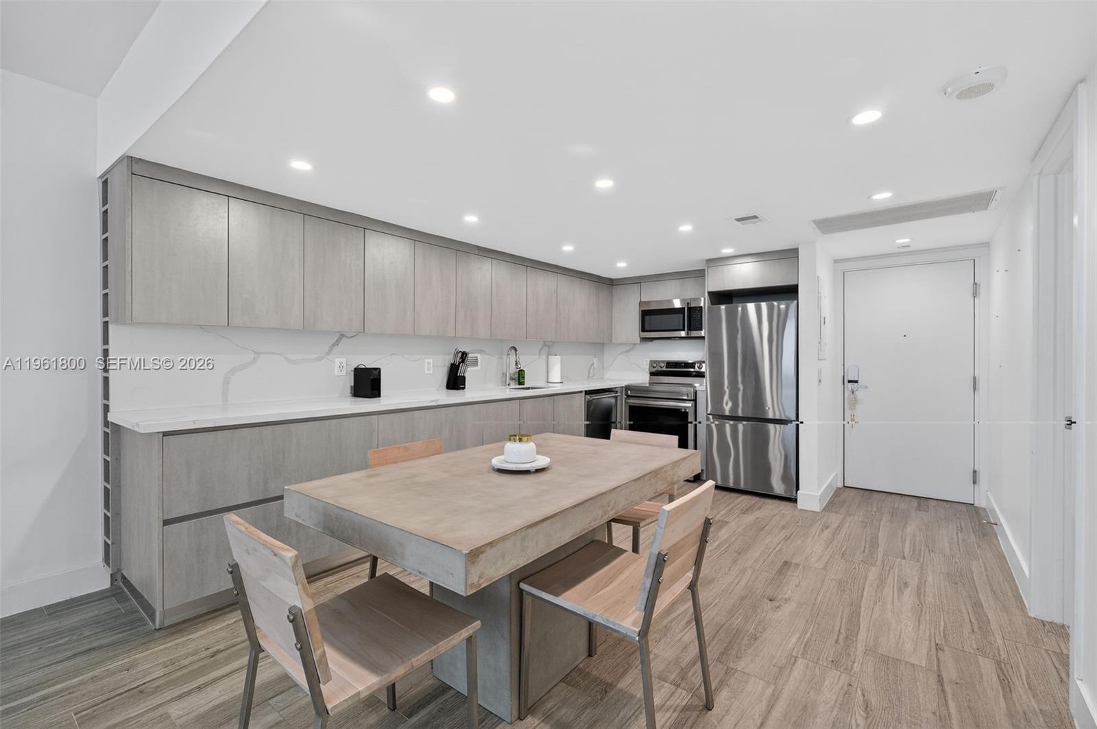 A modern kitchen features light wood cabinetry, a concrete dining table, and stainless steel appliances — 2301 Collins Ave # 943, Miami Beach FL 33139, MIAMI BEACH, FL