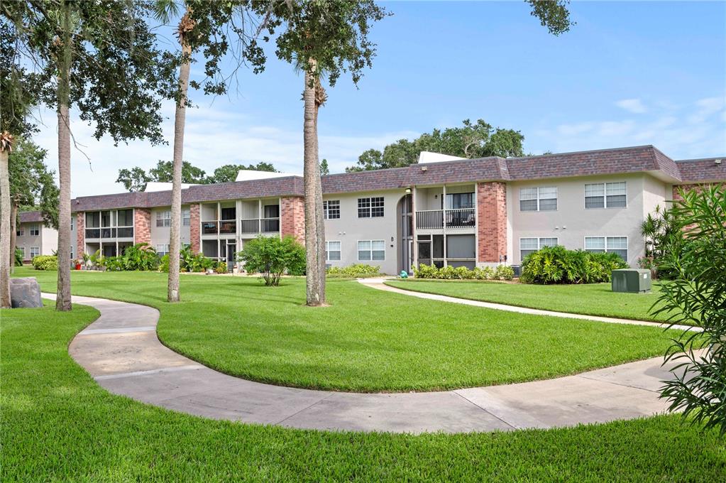 A two-story apartment building with brick accents and a curved sidewalk on a grassy lawn — 3800 SAXON DRIVE UNIT 19B, NEW SMYRNA BEACH, FL