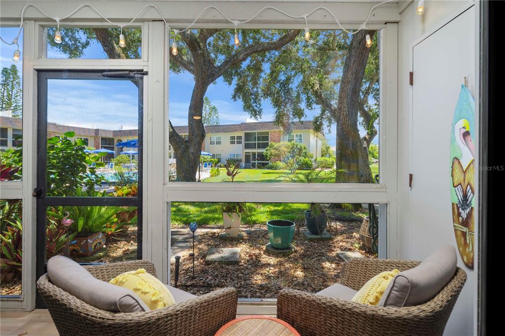 A screened-in porch features two wicker chairs overlooking a grassy courtyard with a swimming pool — 3800 SAXON DRIVE UNIT 19B, NEW SMYRNA BEACH, FL
