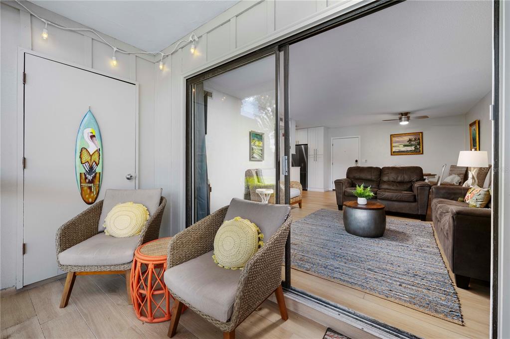A patio with two wicker chairs overlooks a living room with a brown sofa — 3800 SAXON DRIVE UNIT 19B, NEW SMYRNA BEACH, FL