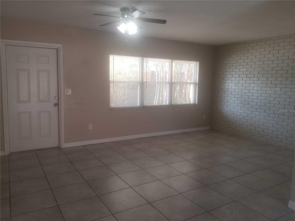 A living room features light-colored tile flooring, a white brick wall, and a ceiling fan — 3366 CAMELOT DRIVE UNIT A & B, LARGO, FL