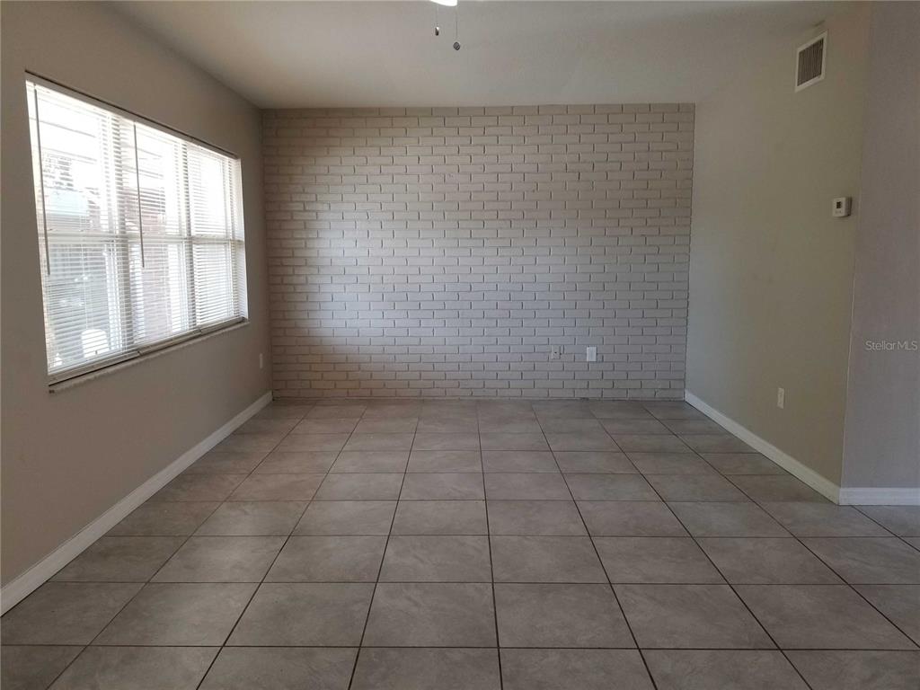An empty room features a light-colored brick accent wall, large tile flooring, and a window — 3366 CAMELOT DRIVE UNIT A & B, LARGO, FL