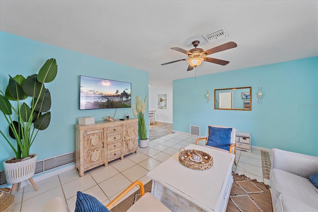 A living room with light blue walls, tile flooring, a ceiling fan, and coastal decor — 108 STANFORD ROAD, VENICE, FL