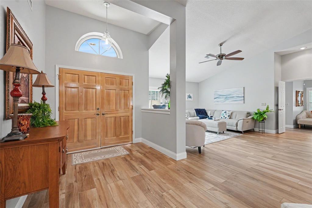 A bright entryway with wood-look flooring leads into a living room with a ceiling fan — 2782 SCOBEE DRIVE, PALM HARBOR, FL