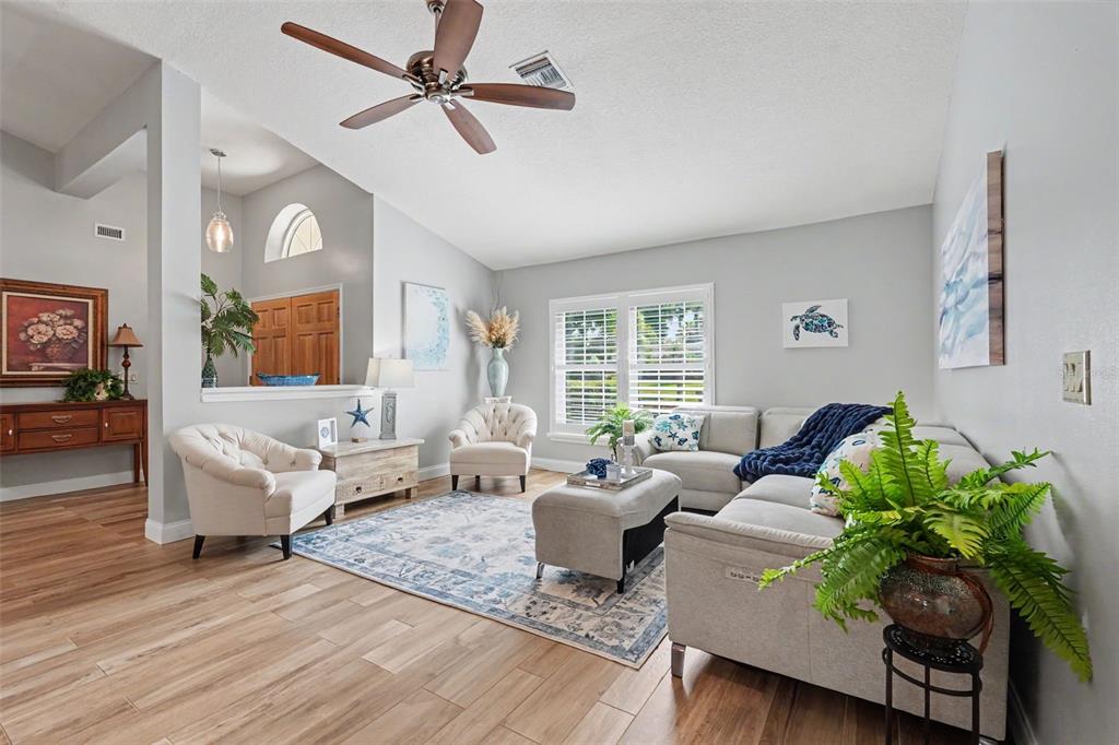 A bright living room features light wood-look tile floors, a ceiling fan, and neutral furniture — 2782 SCOBEE DRIVE, PALM HARBOR, FL