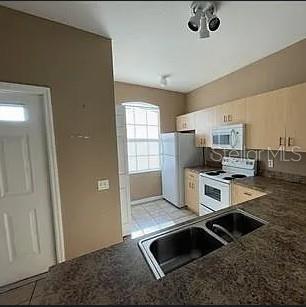 A kitchen features light wood cabinets, dark countertops, a double sink, and white appliances — 13102 INDIAN CREEK DRIVE UNIT 0, POINCIANA, FL