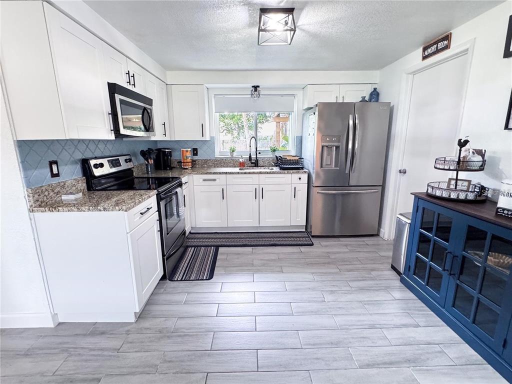 A kitchen features white cabinets, stainless steel appliances, granite countertops, and light gray tile flooring — 9616 PINE RIDGE AVENUE, RIVERVIEW, FL