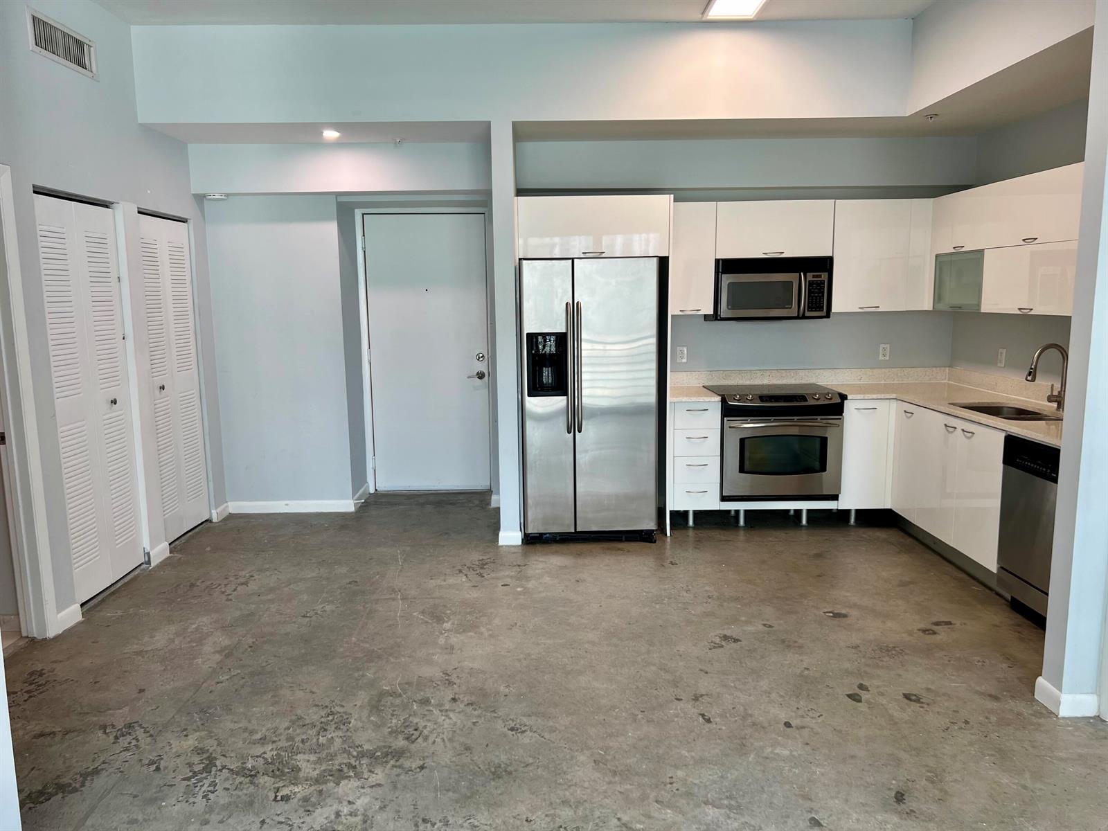 A kitchen with white cabinets, stainless steel appliances, and concrete flooring in an open space — 133 NE 2nd Avenue # 1006, Miami FL 33132, MIAMI, FL