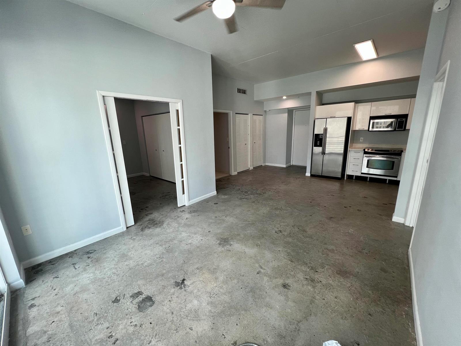An open-concept living area features gray walls, a concrete floor, and an adjacent kitchen — 133 NE 2nd Avenue # 1006, Miami FL 33132, MIAMI, FL
