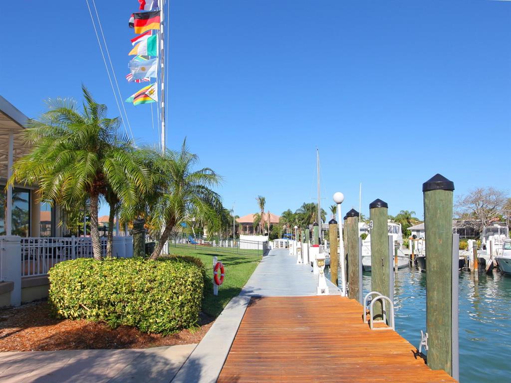 A wooden dock extends toward a marina with boats under a clear blue sky — 509 SPOONBILL WAY, SARASOTA, FL