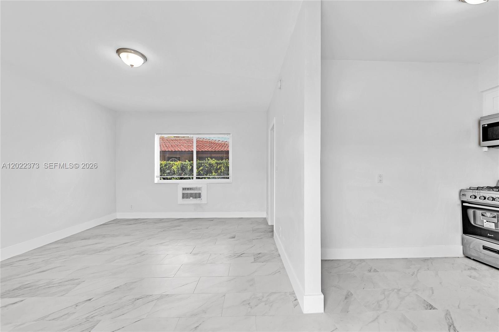 A bright room with white walls, marble-patterned tile flooring, and an adjacent kitchen area — 1839 Funston St # 6, Hollywood FL 33020, HOLLYWOOD, FL