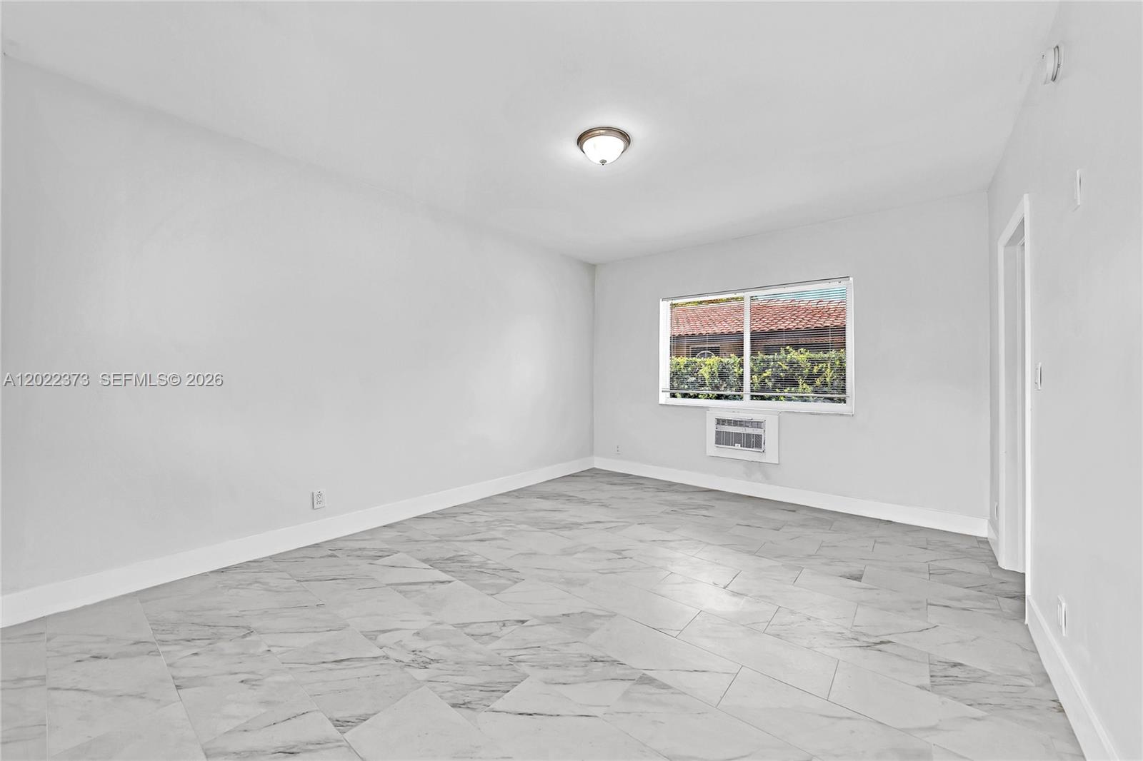 An empty room features light gray marble-look tile flooring, white walls, and a window unit — 1839 Funston St # 6, Hollywood FL 33020, HOLLYWOOD, FL
