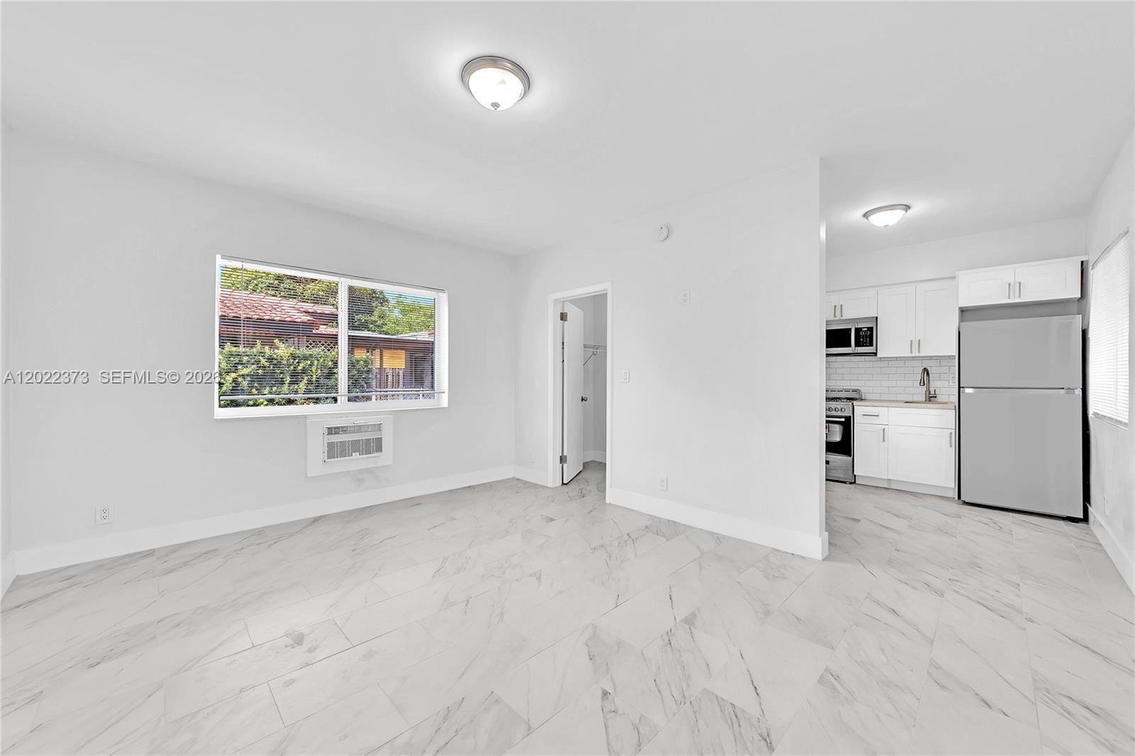 A bright room features white walls, marble-patterned tile flooring, and an adjacent galley kitchen — 1839 Funston St # 6, Hollywood FL 33020, HOLLYWOOD, FL