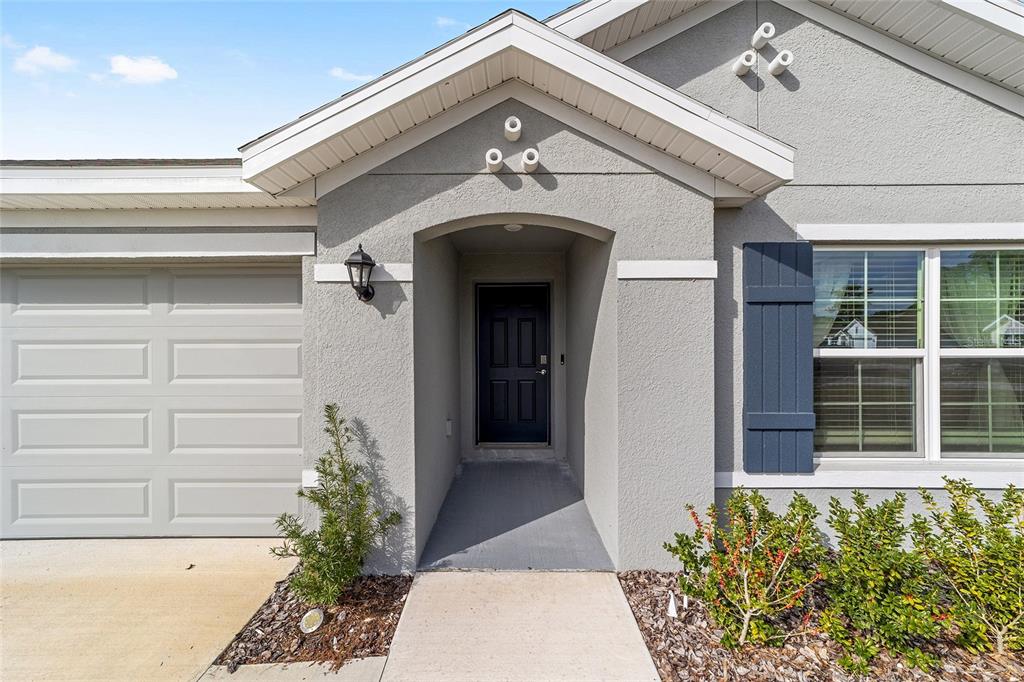 The exterior of a house features a gray stucco facade, a dark door, and shutters — 7199 SW 135TH PLACE, OCALA, FL