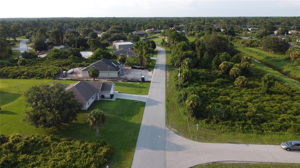 An aerial view shows a paved road leading past residential houses and dense wooded areas — Lot 30 CLOVELON STREET, NORTH PORT, FL