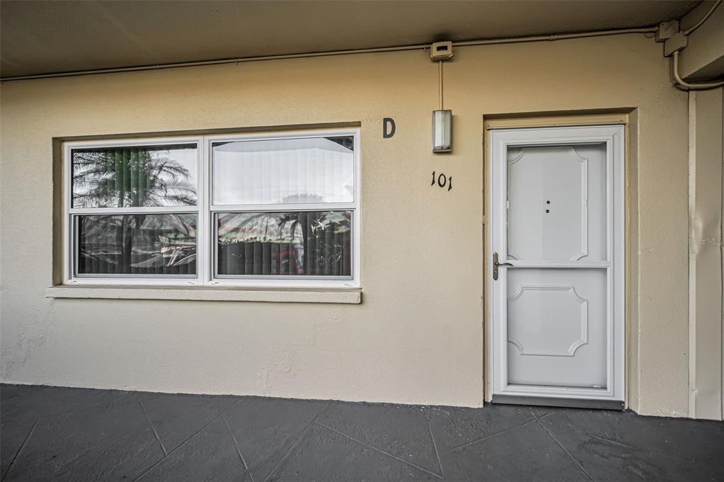 A beige exterior wall features a window, a white storm door, and unit number 101 — 5750 80TH STREET N UNIT D101, ST PETERSBURG, FL