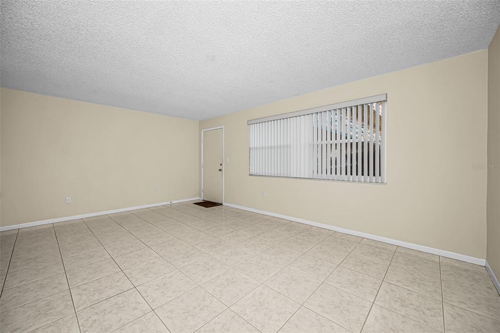 An empty room with beige walls, tile flooring, and a window with vertical blinds — 5750 80TH STREET N UNIT D101, ST PETERSBURG, FL