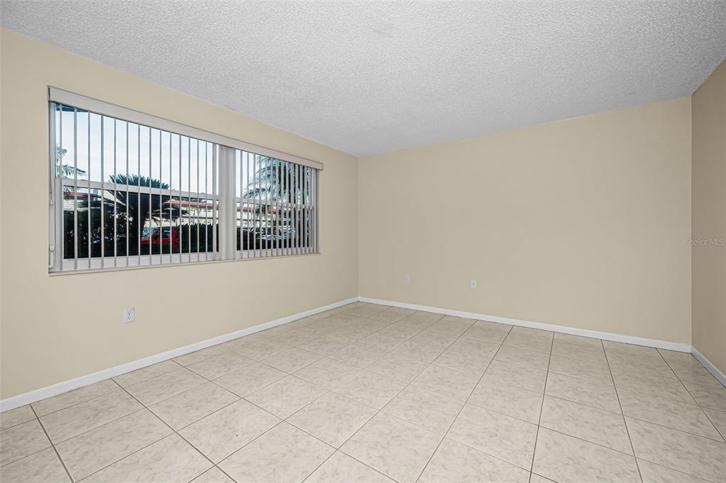 An empty room features beige walls, white trim, and light-colored square floor tiles — 5750 80TH STREET N UNIT D101, ST PETERSBURG, FL
